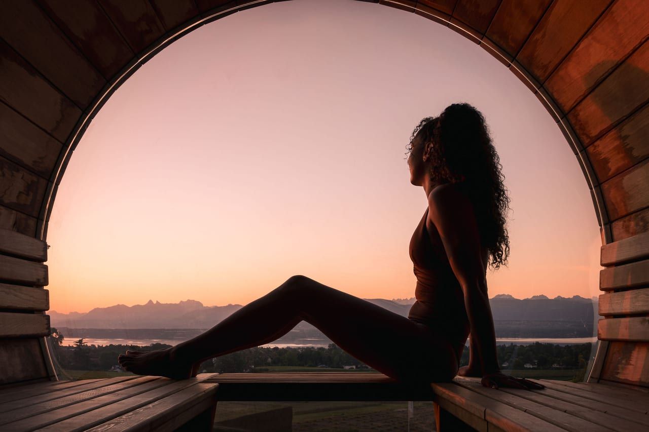 Silhouette dans la fenêtre ronde du sauna, face au lac au coucher du soleil